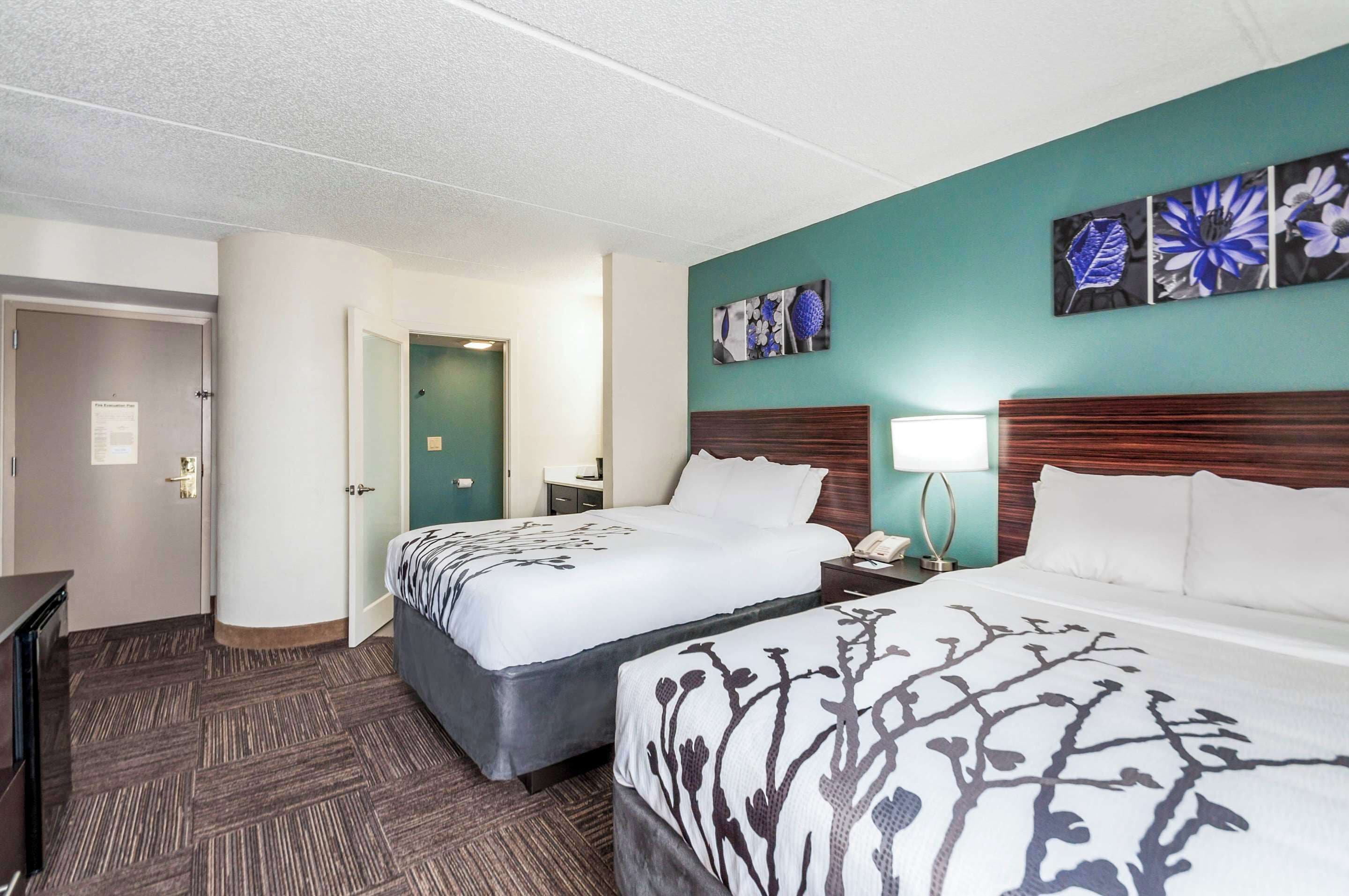 Een hotelkamer met twee bedden, een houten hoofdbord, een nachtkastje met een lamp en kunst aan de muur.