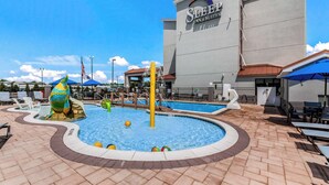 A swimming pool area with a mermaid statue, lounge chairs, and a Sleep Inn & Suites building in the background.