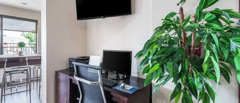 A modern office space with a desk, computer, and a large monitor. There is a chair and a potted plant.