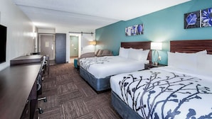 A hotel room with two beds, a desk, a chair, and a TV.