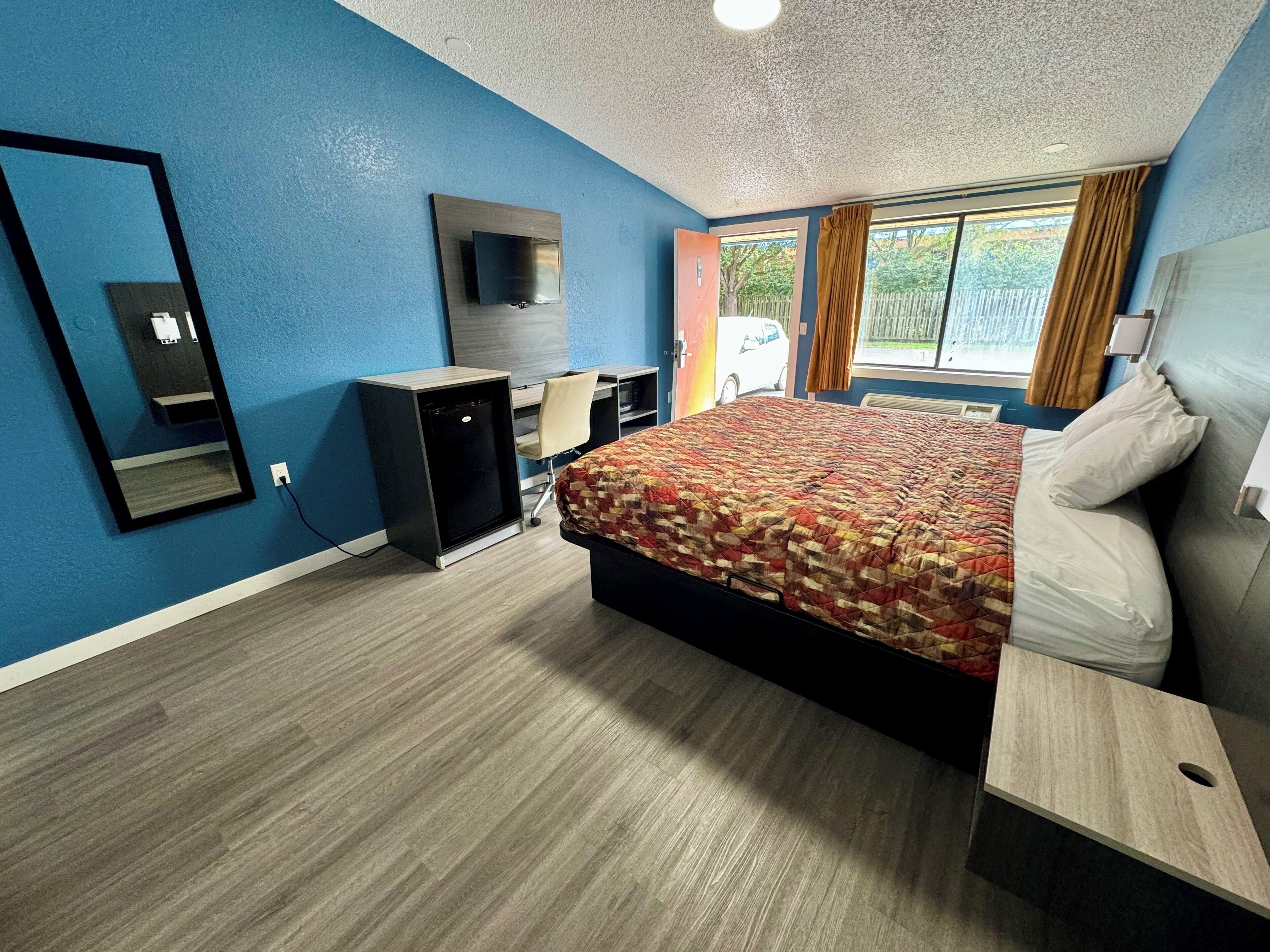 A hotel room with a bed, a desk, a TV, and a window with curtains.
