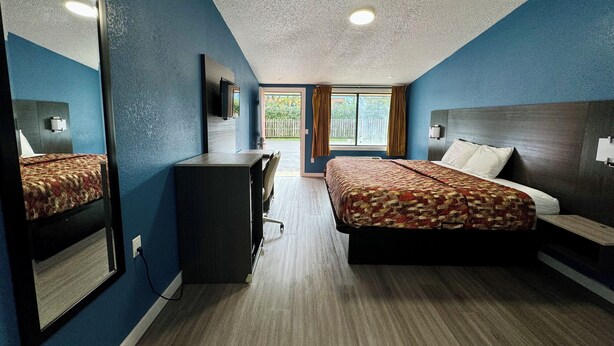 A hotel room with a bed, a desk, a chair, a television, and a window with curtains. - Knights Inn Greenville, NC (Greenville)