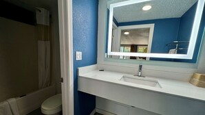 A bathroom with a white sink, blue walls, and a mirror with a lighted frame. - Knights Inn Greenville, NC (Greenville)