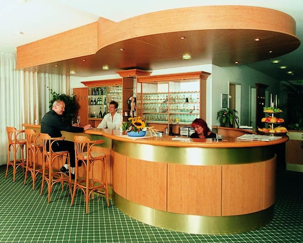Un espace d’accueil d’hôtel avec un comptoir incurvé, des chaises en bois et un sol à carreaux verts.