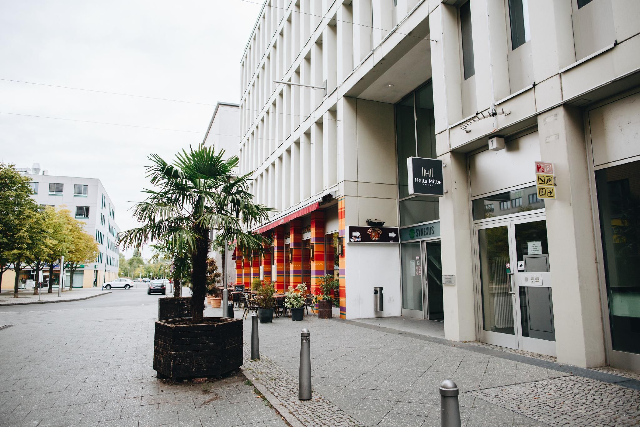 Ein modernes Gebäude mit einem Hotelschild, einem farbenfrohen Geschäft und einem Palmenbeet.
