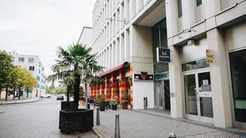 Ein modernes Gebäude mit einem Hotelschild, einem farbenfrohen Geschäft und einem Palmenbeet.