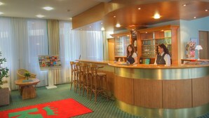 A hotel reception area with a curved counter, wooden chairs, a red carpet, and a bulletin board. - Kubrat In Helle Mitte (Berlin)