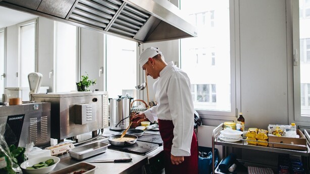 A chef preparing food in a modern kitchen with stainless steel appliances and large windows. - Kubrat In Helle Mitte (Berlin)
