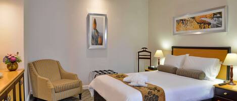 A hotel room with a bed, a chair, a bedside table, a lamp, and a picture on the wall.