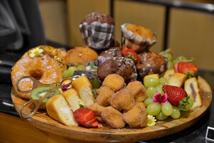 A wooden board with various pastries, fruits, and a pair of scissors.