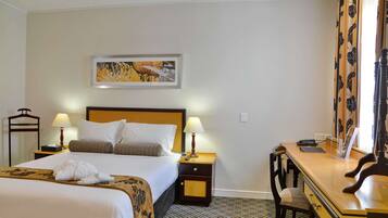 Habitación de hotel con cama, mesitas de noche, un escritorio, una silla, una lámpara, un cuadro en la pared y un suelo estampado.