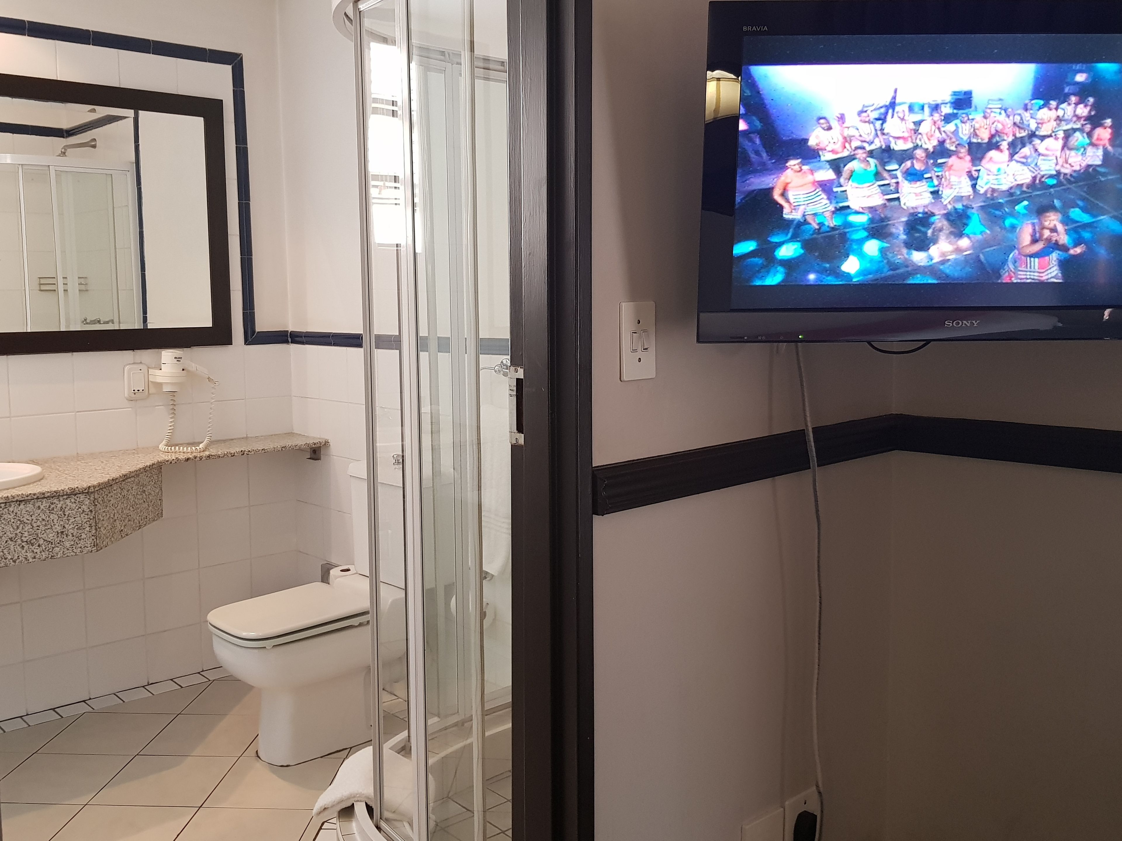 Un baño con ducha, inodoro y televisor montado en la pared.