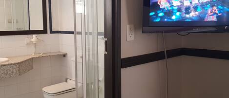 Un baño con ducha, inodoro y televisor montado en la pared.