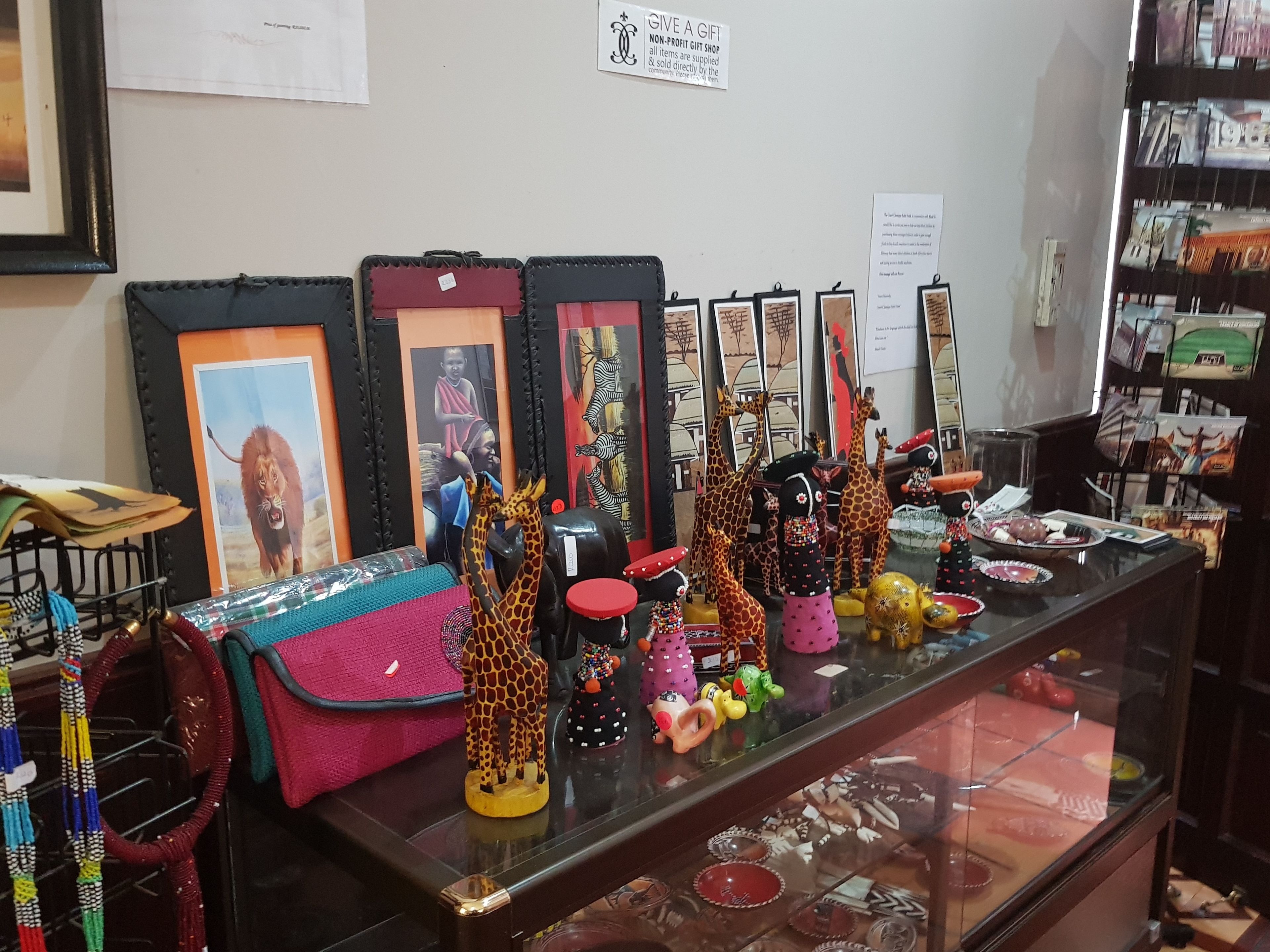 A display of various items including framed pictures, colorful bags, and decorative figurines on a glass counter.