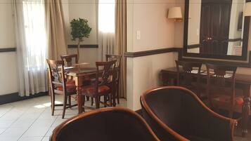Een hotelkamer met een eethoek, bestaande uit een houten tafel en stoelen, een potplant en een grote spiegel aan de muur.
