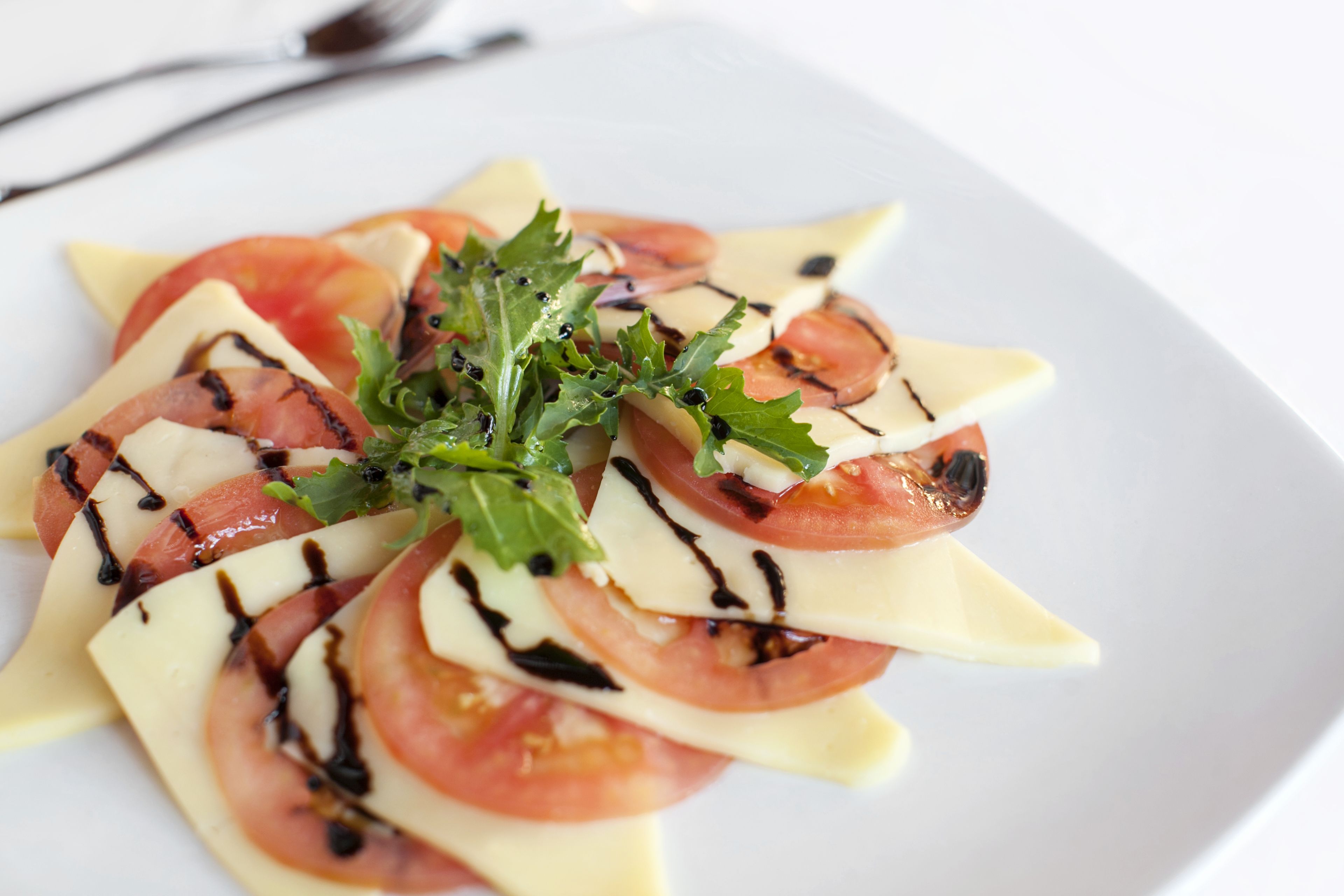 A plate of food with grilled tomatoes, cheese, and greens, served on a white plate.