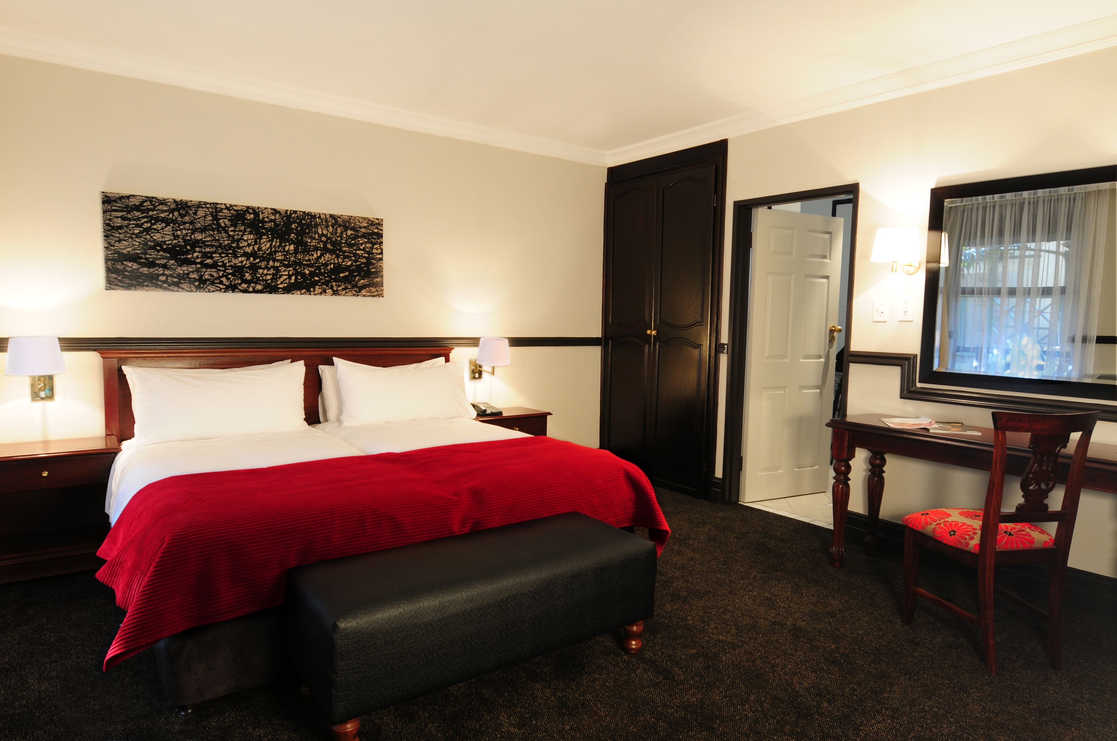 Habitación de hotel con una cama grande, un banco, un escritorio con una silla, un televisor y una puerta que da a un baño.