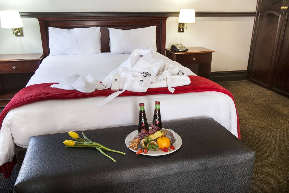 Ein ordentlich bezogenes Bett mit weißen Laken, einer roten Decke und einem Tablett mit Obst und Getränken.