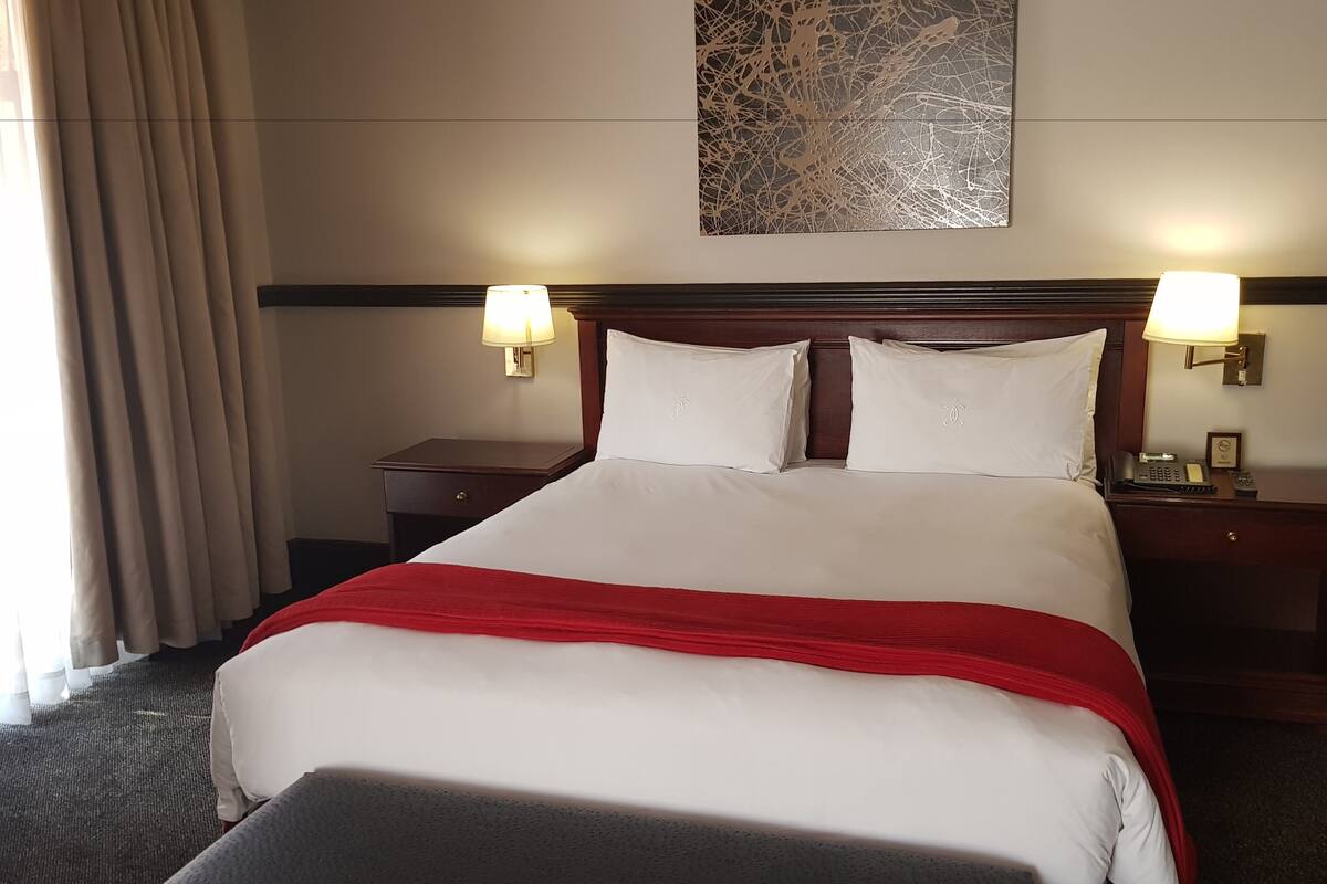 Ein Hotelzimmer mit einem großen Bett, zwei Nachttischlampen, einem Kopfteil und einem Wandbild.