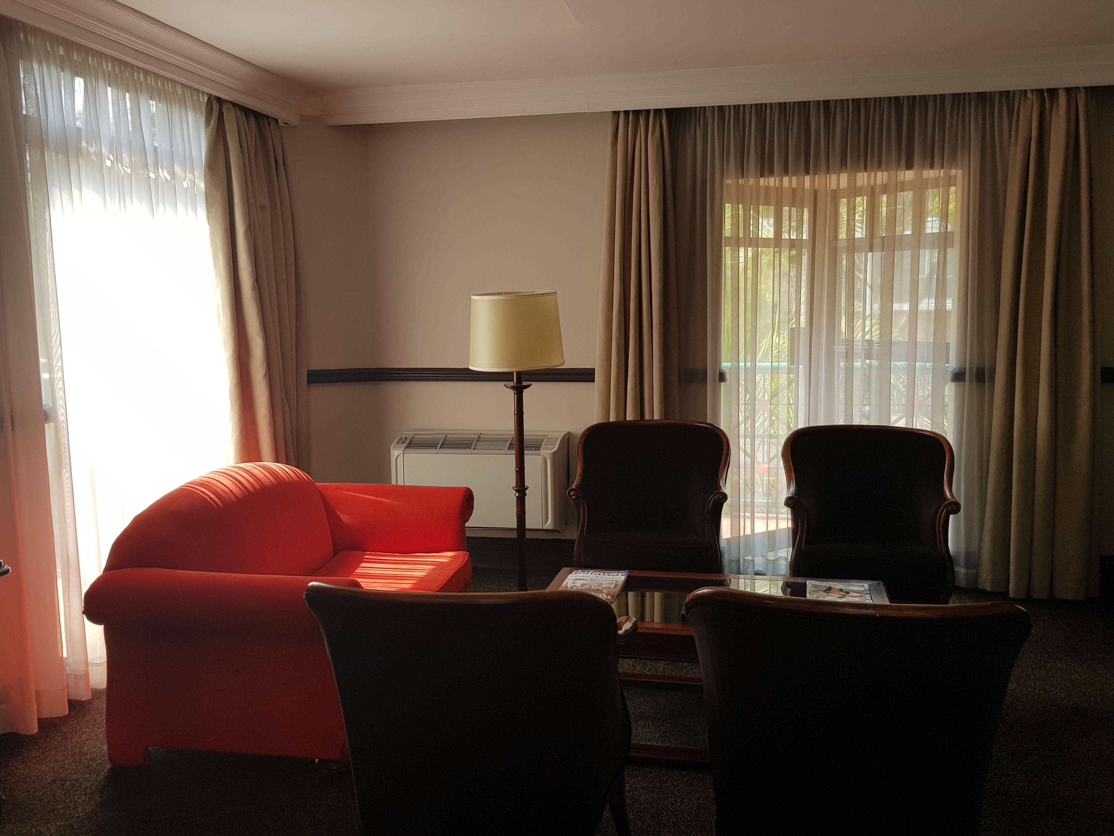 A hotel room with a red sofa, two armchairs, a small table, a lamp, and a window with curtains.