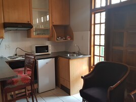 Una cocina compacta con armarios de madera, un microondas, un refrigerador pequeño y un lavamanos.
