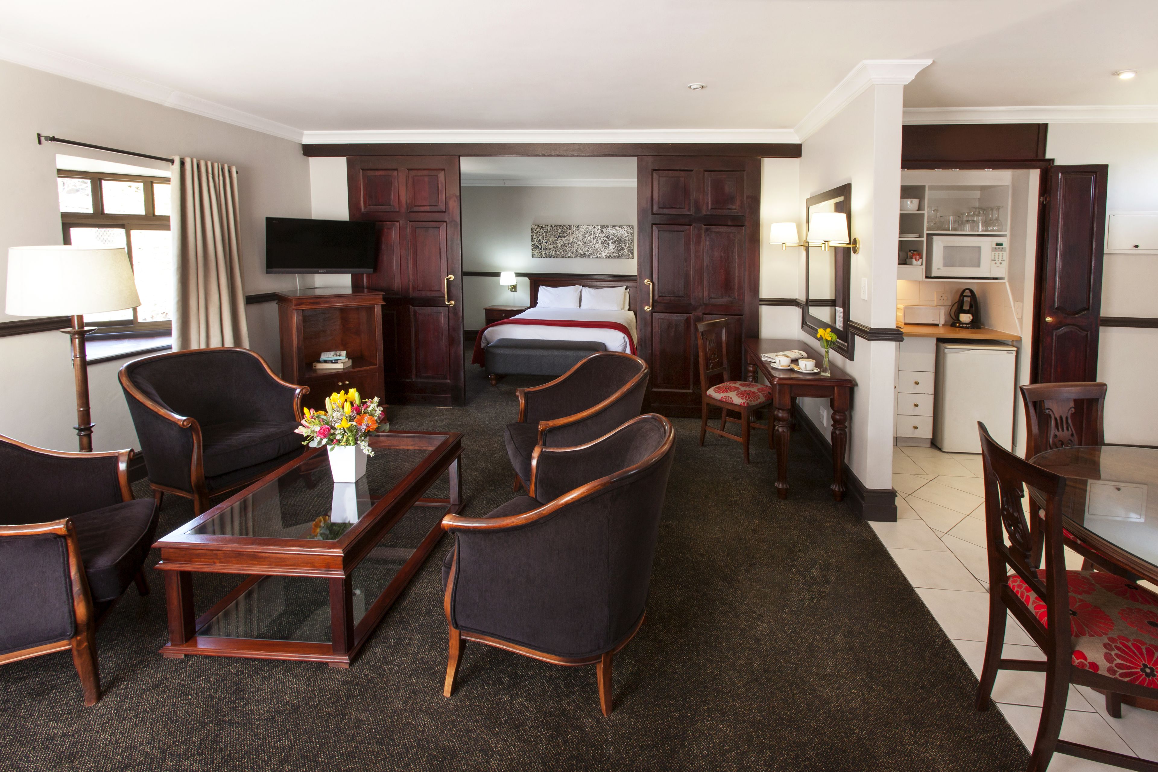 A hotel room with a bed, a TV, a desk, a chair, a coffee maker, and a small kitchen area.