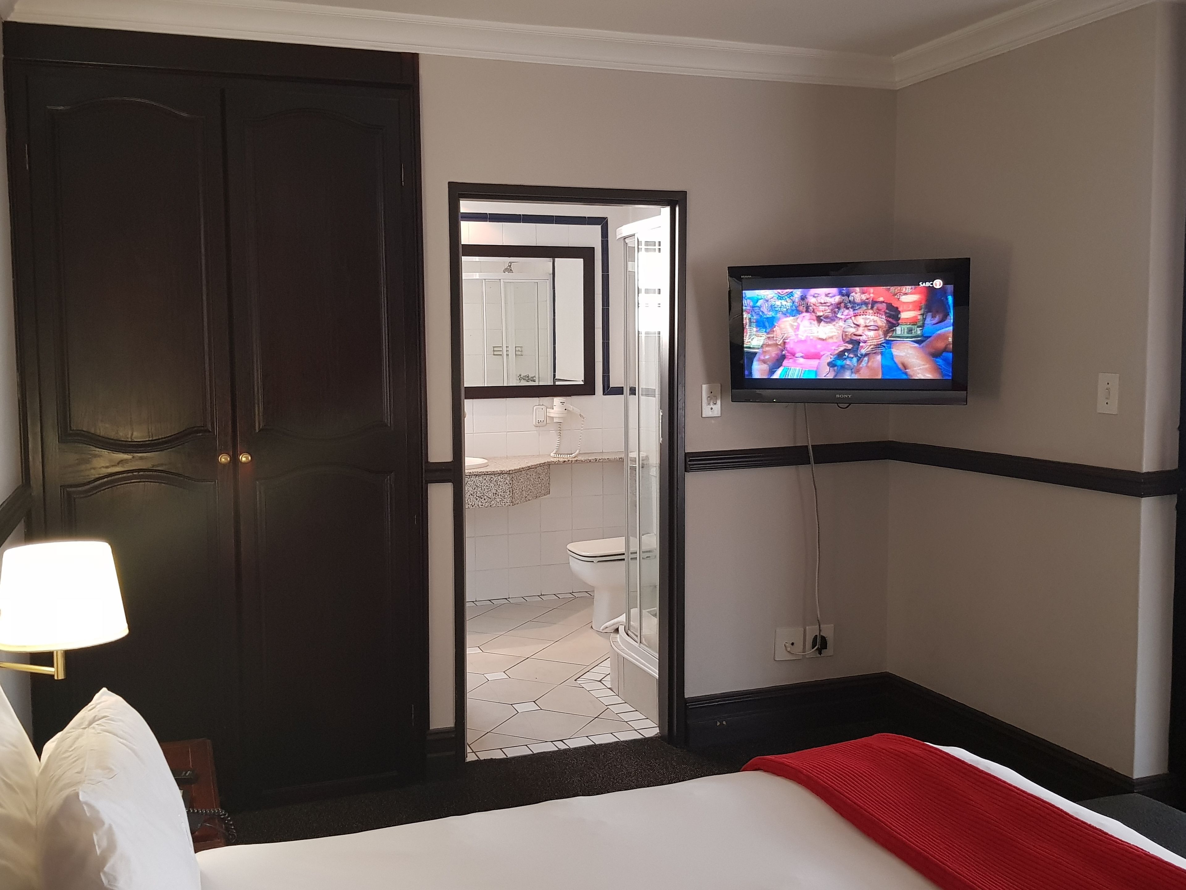 A hotel room with a bed, a TV mounted on the wall, a door, and a bathroom visible through an open door.