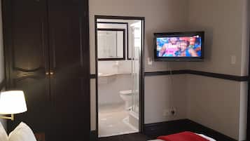 A hotel room with a bed, a TV mounted on the wall, a door, and a bathroom visible through an open door.