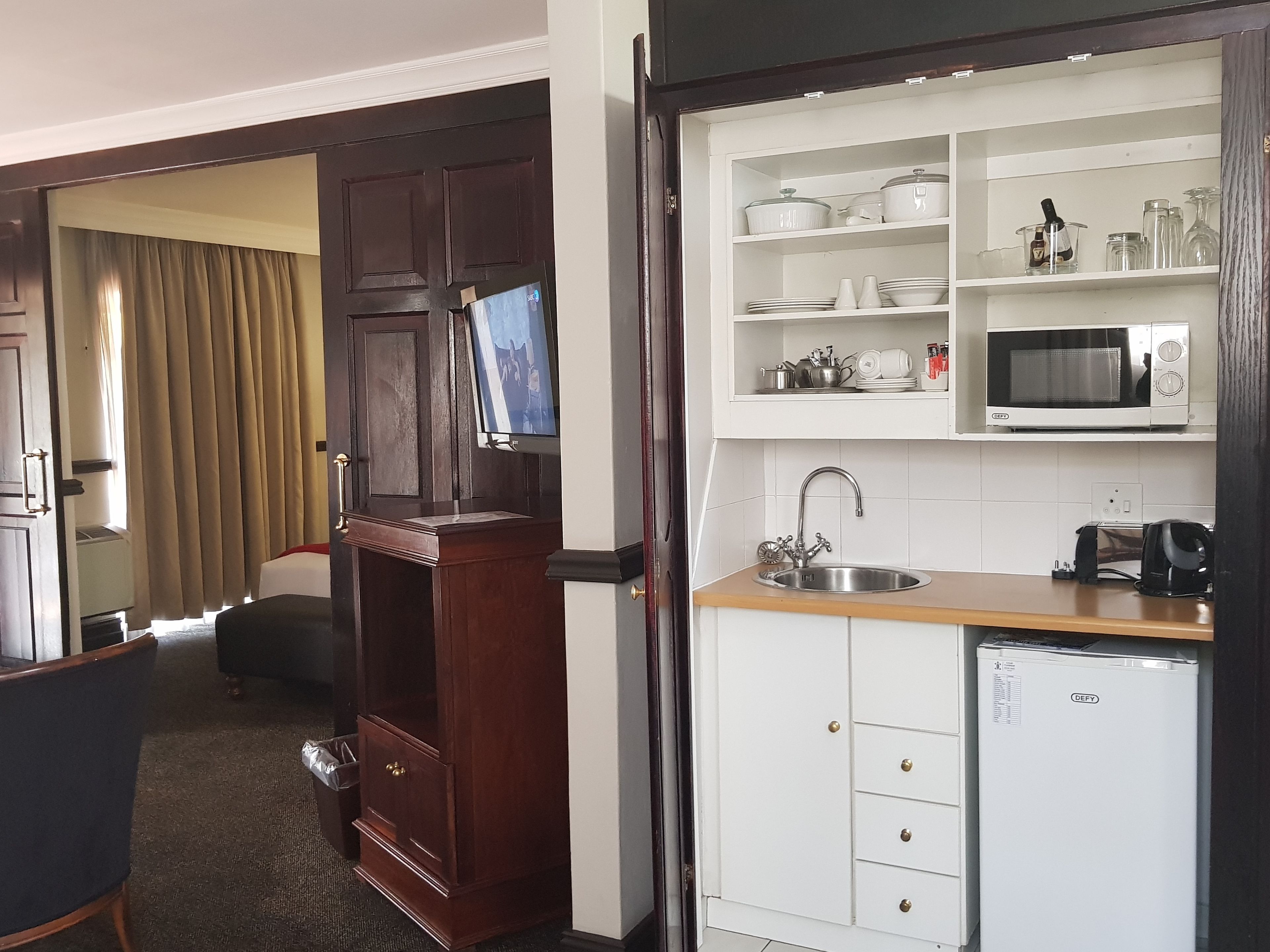 Ein Hotelzimmer mit Holzschrank, einer kleinen Küchenzeile mit Mikrowelle, Spüle und Minikühlschrank.