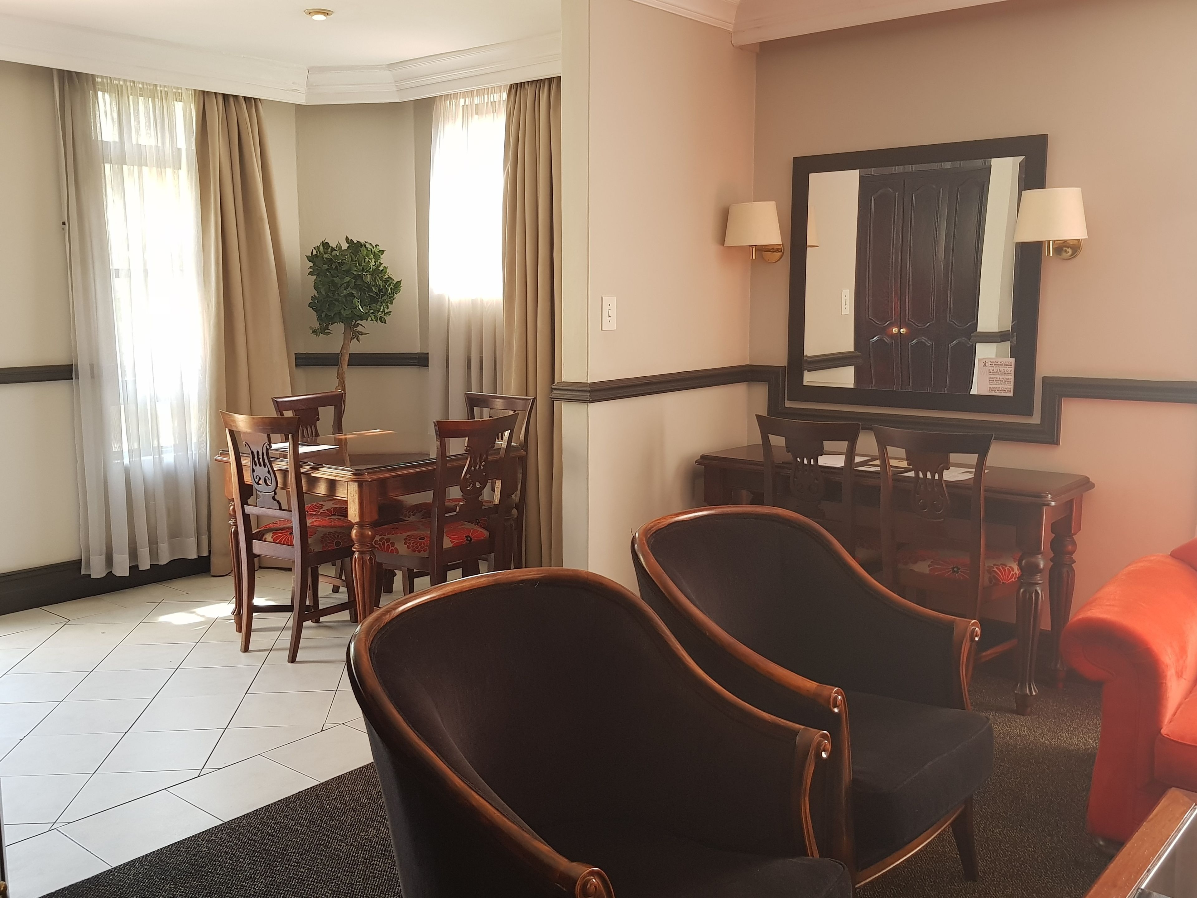 A hotel room with a dining area, two armchairs, a table, and a potted plant.