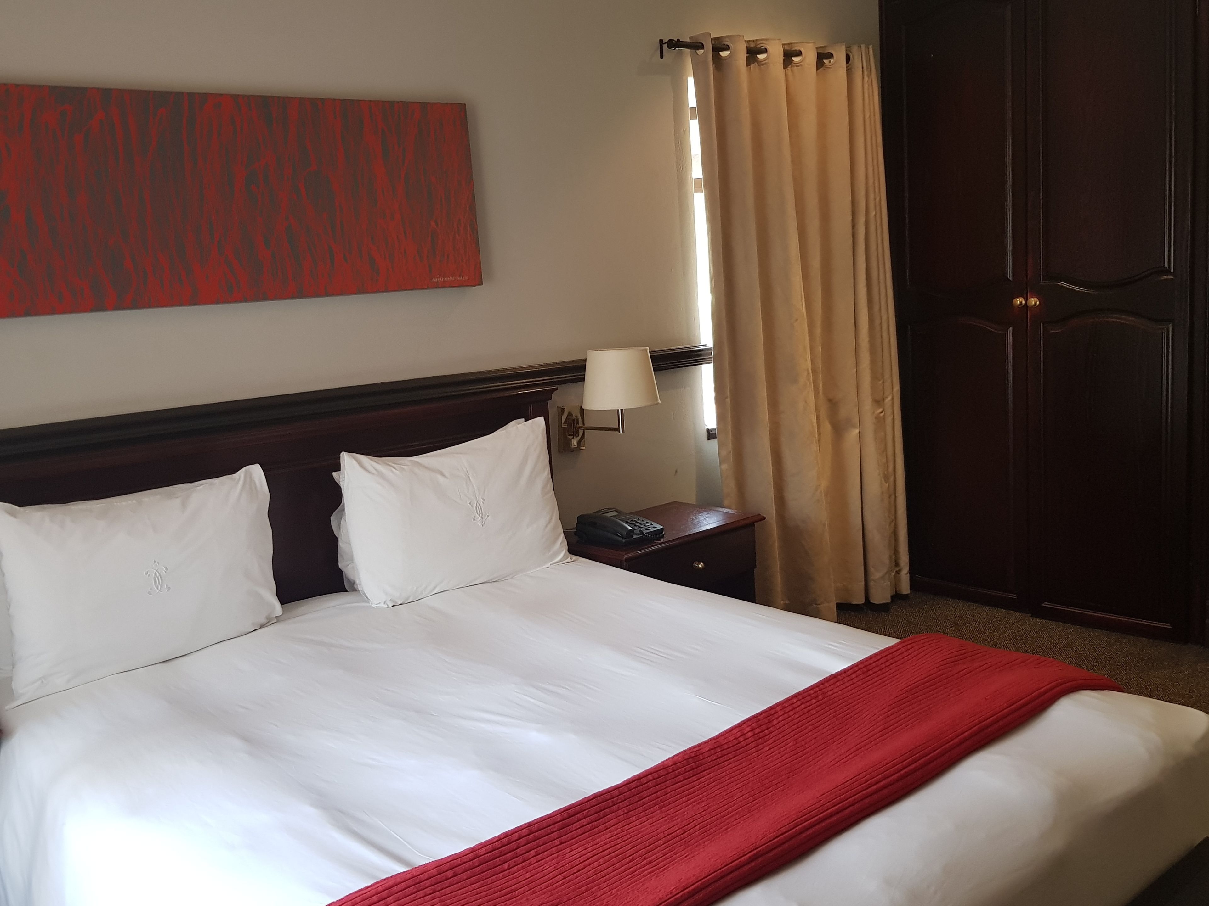 Une chambre d’hôtel avec un grand lit, une table de chevet avec une lampe, un téléphone et une armoire.