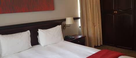 Une chambre d’hôtel avec un grand lit, une table de chevet avec une lampe, un téléphone et une armoire.