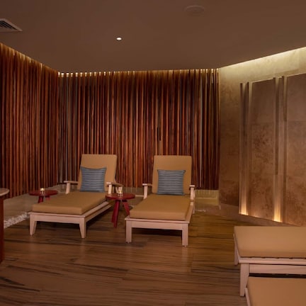 A spa room with two lounge chairs, a small table, and a decorative vase with flowers.