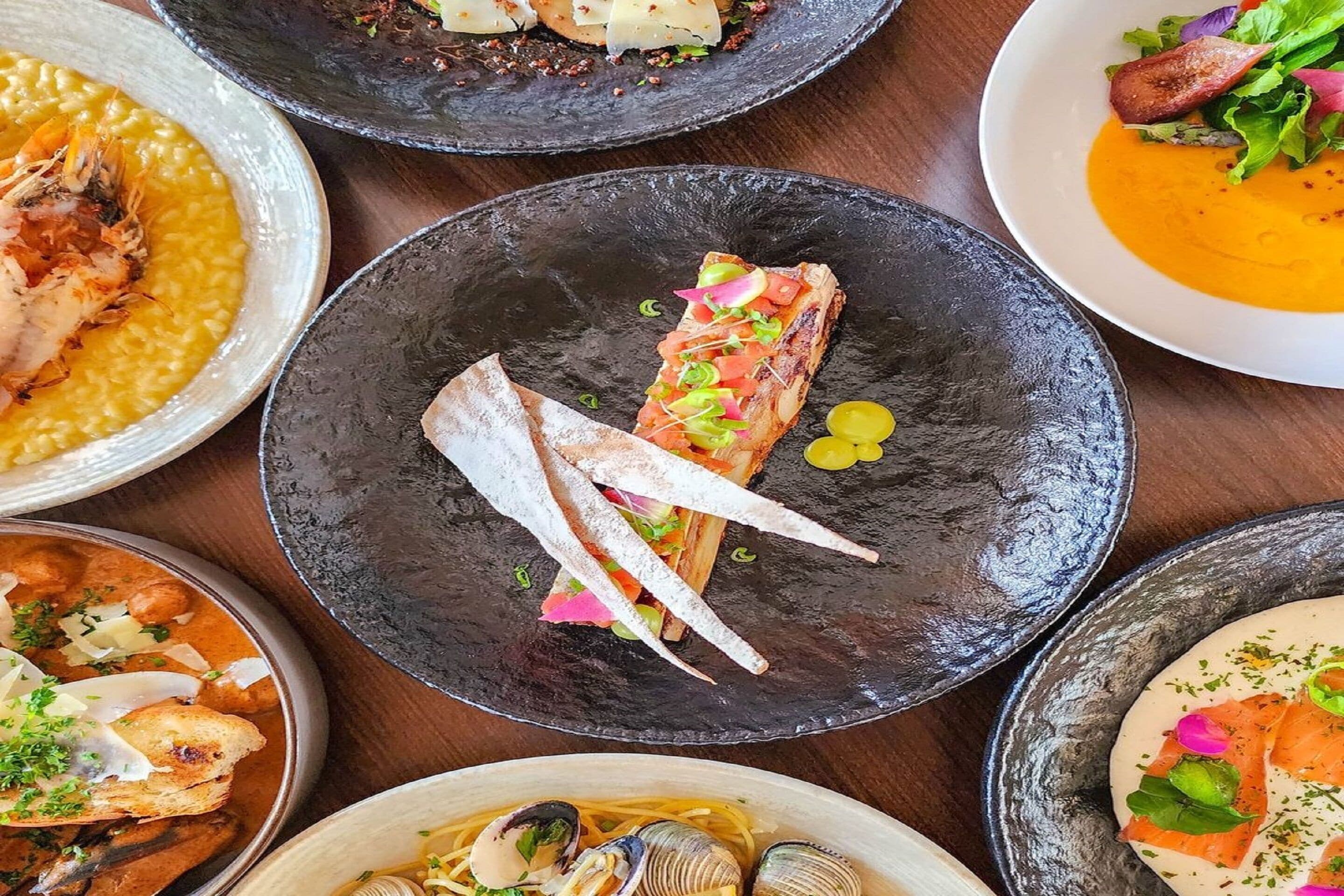 Diversos platos sobre una mesa de madera, incluyendo mariscos y pasta.