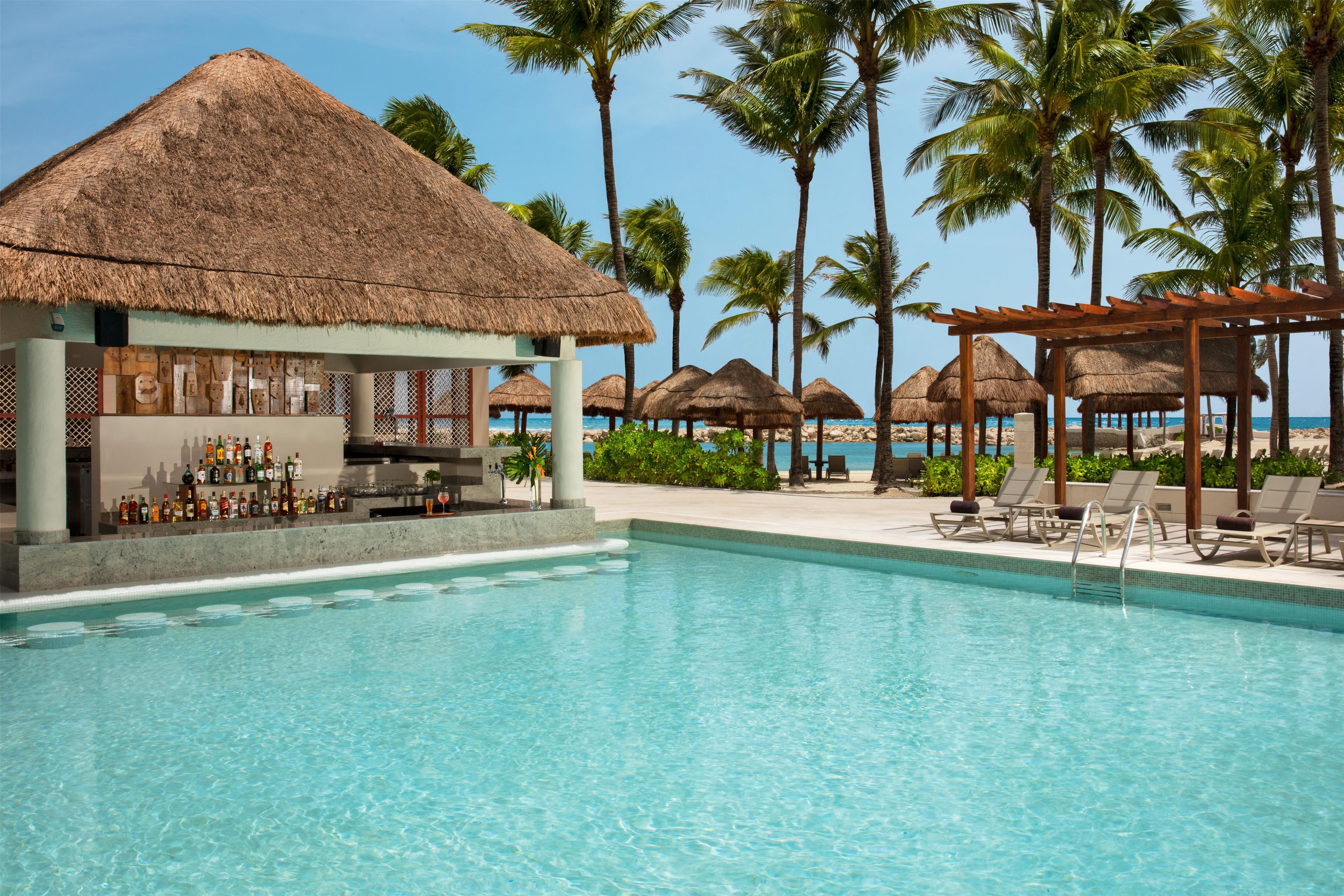 A pool area with a bar, lounge chairs, and thatched umbrellas.
