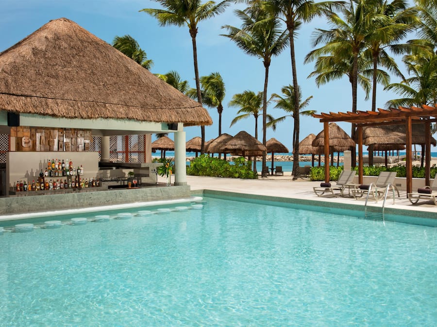 A pool area with a bar, lounge chairs, and thatched umbrellas.