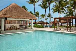 Zona de piscina con bar, sillones reclinables y sombrillas de paja.