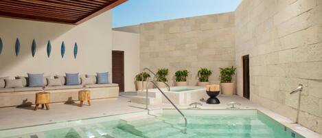 A pool area with a wooden ceiling, a seating area with cushions, and potted plants.