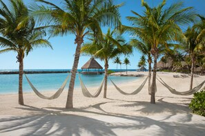 A beach with palm trees, a thatched-roof structure, and a clear blue sky.