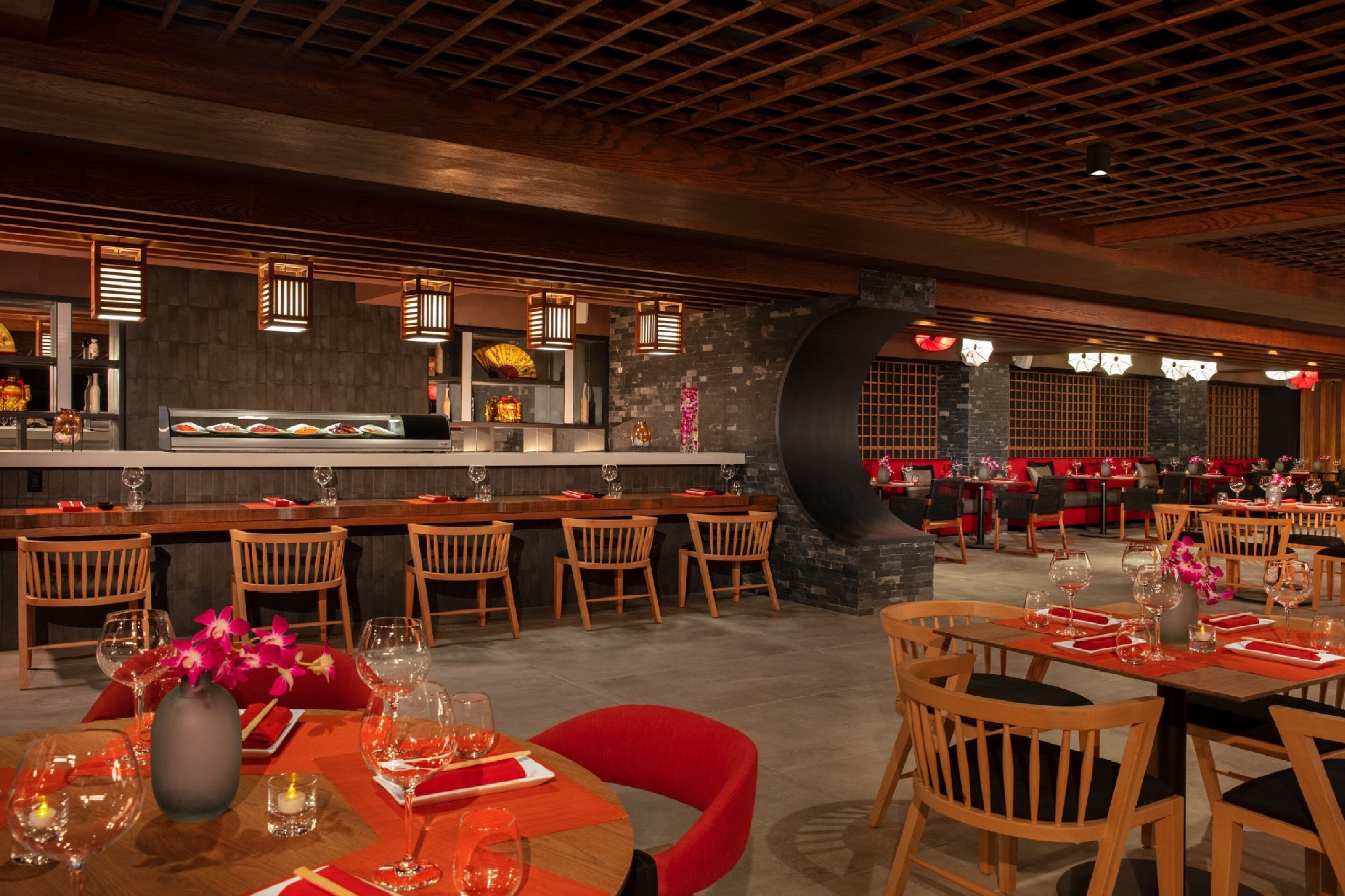 A restaurant with wooden tables and chairs, a bar area, and a stone wall.