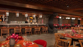 A restaurant with wooden tables and chairs, a bar area, and a stone wall.