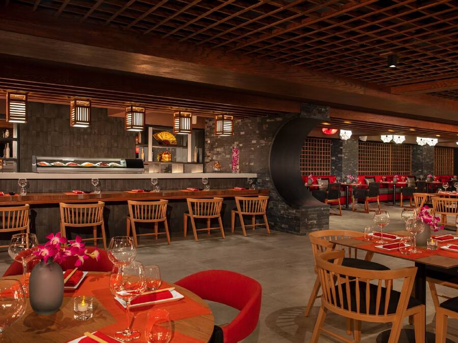 A restaurant with wooden tables and chairs, a bar area, and a stone wall.
