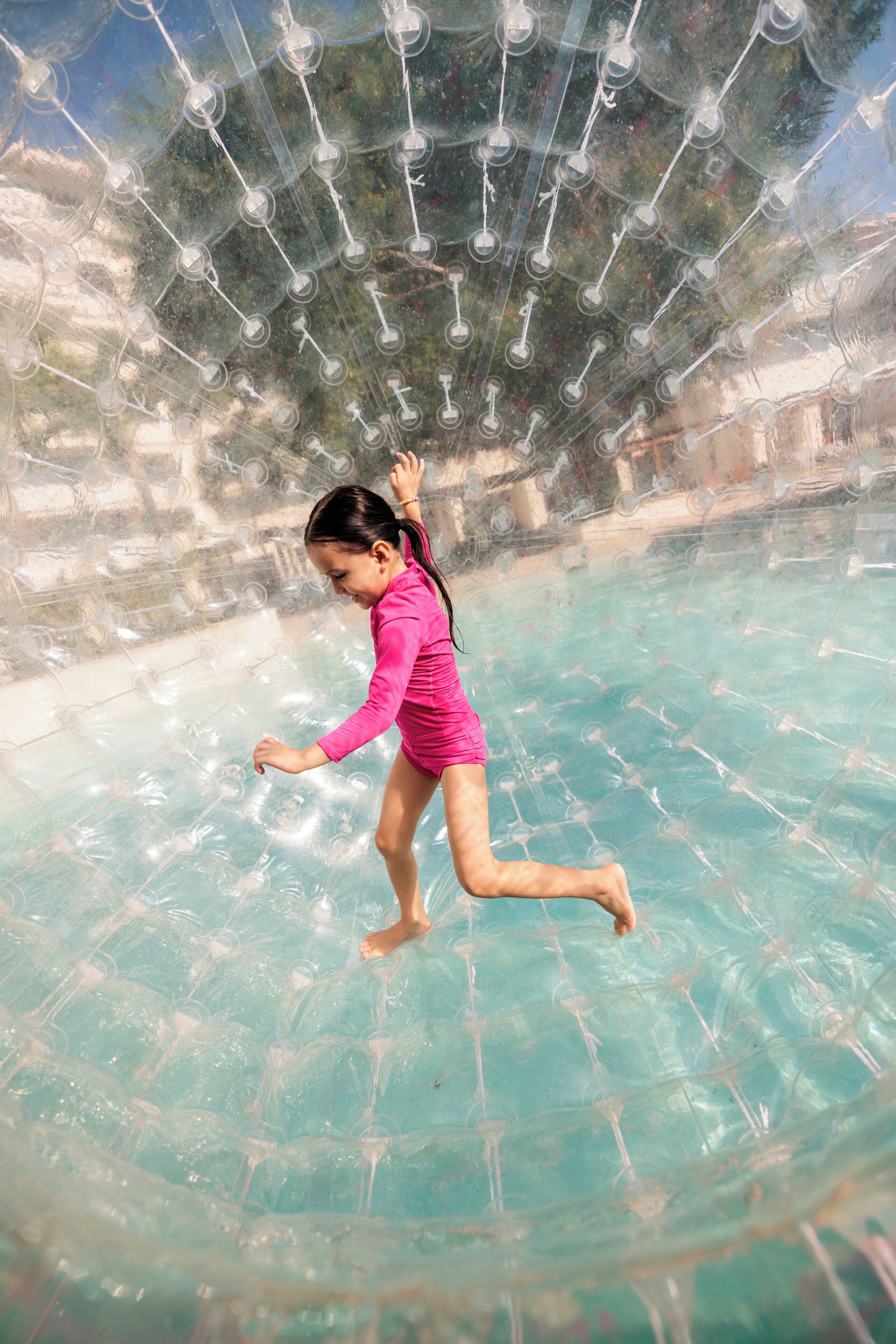Une personne portant un maillot de bain rose se promène à l’intérieur d’une structure transparente en forme de bulle, dans une piscine.