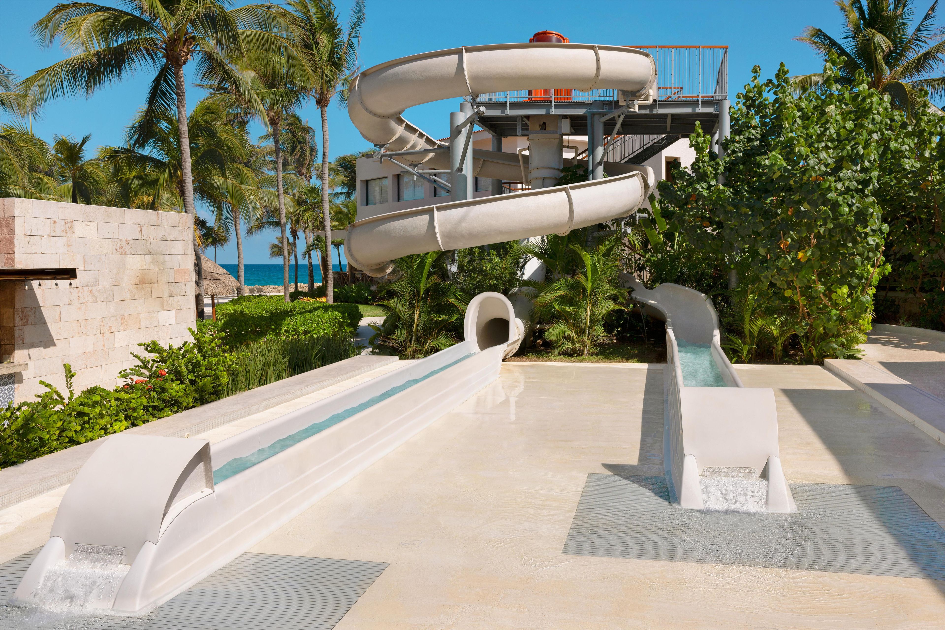 Estructura de toboganes acuáticos con múltiples carriles, zona de piscina y palmeras.