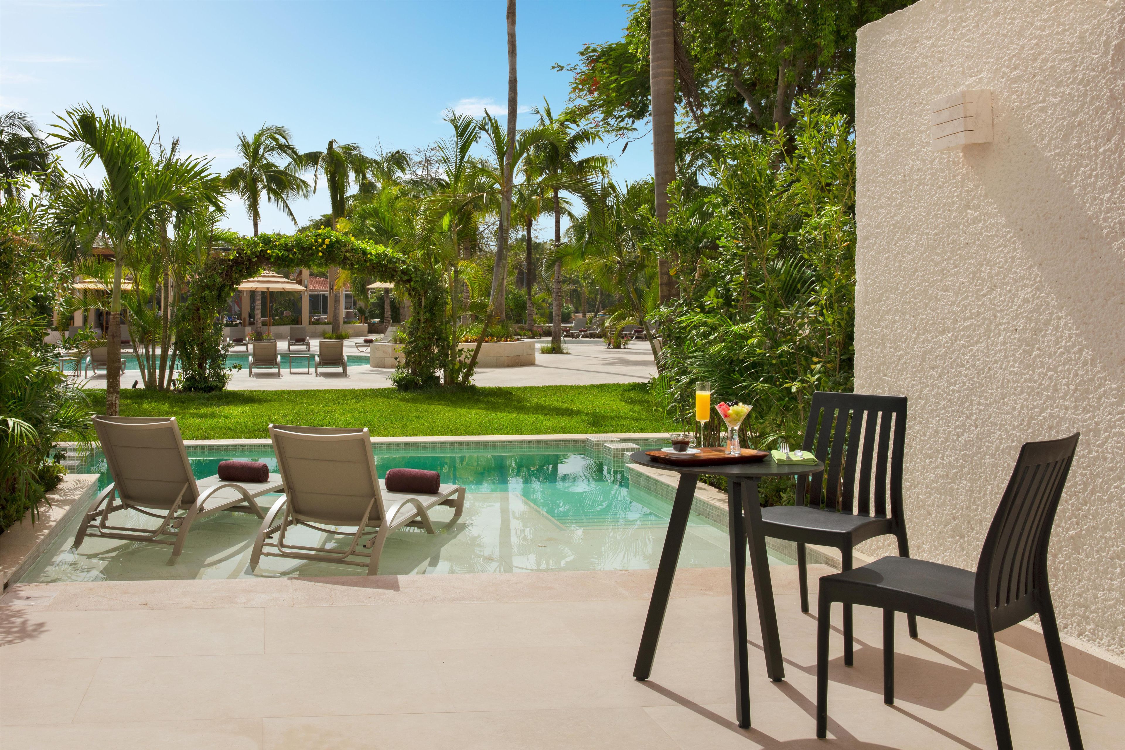 Ein Poolbereich mit Liegestühlen, einem Tisch mit einem Getränk und Blick auf Pool und Garten.