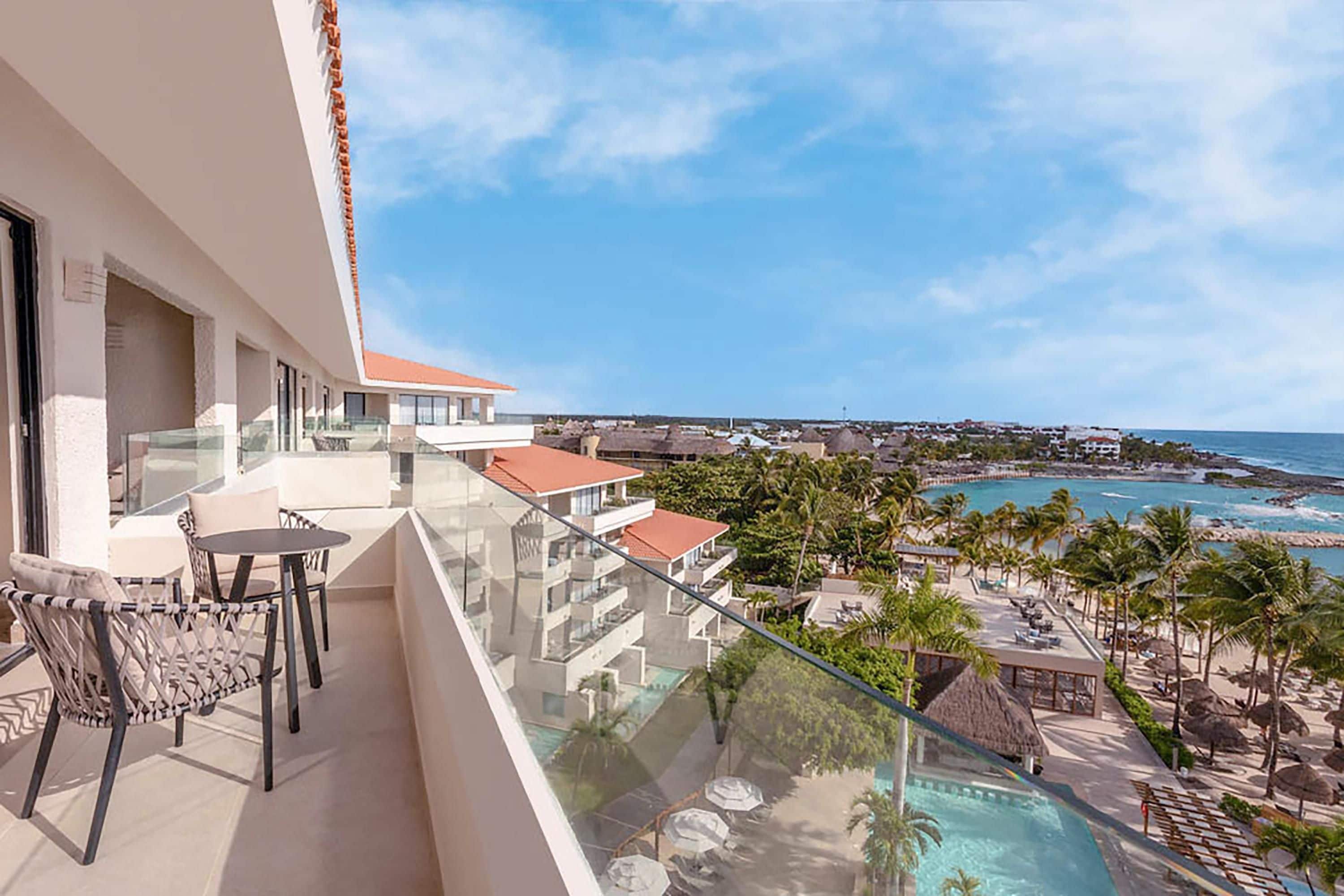 Un balcón con barandilla de cristal con vistas a una piscina y una playa.
