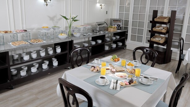 Un bufé de desayuno con diversas opciones de comida y bebidas, una mesa blanca con un mantel individual azul y una silla de madera.