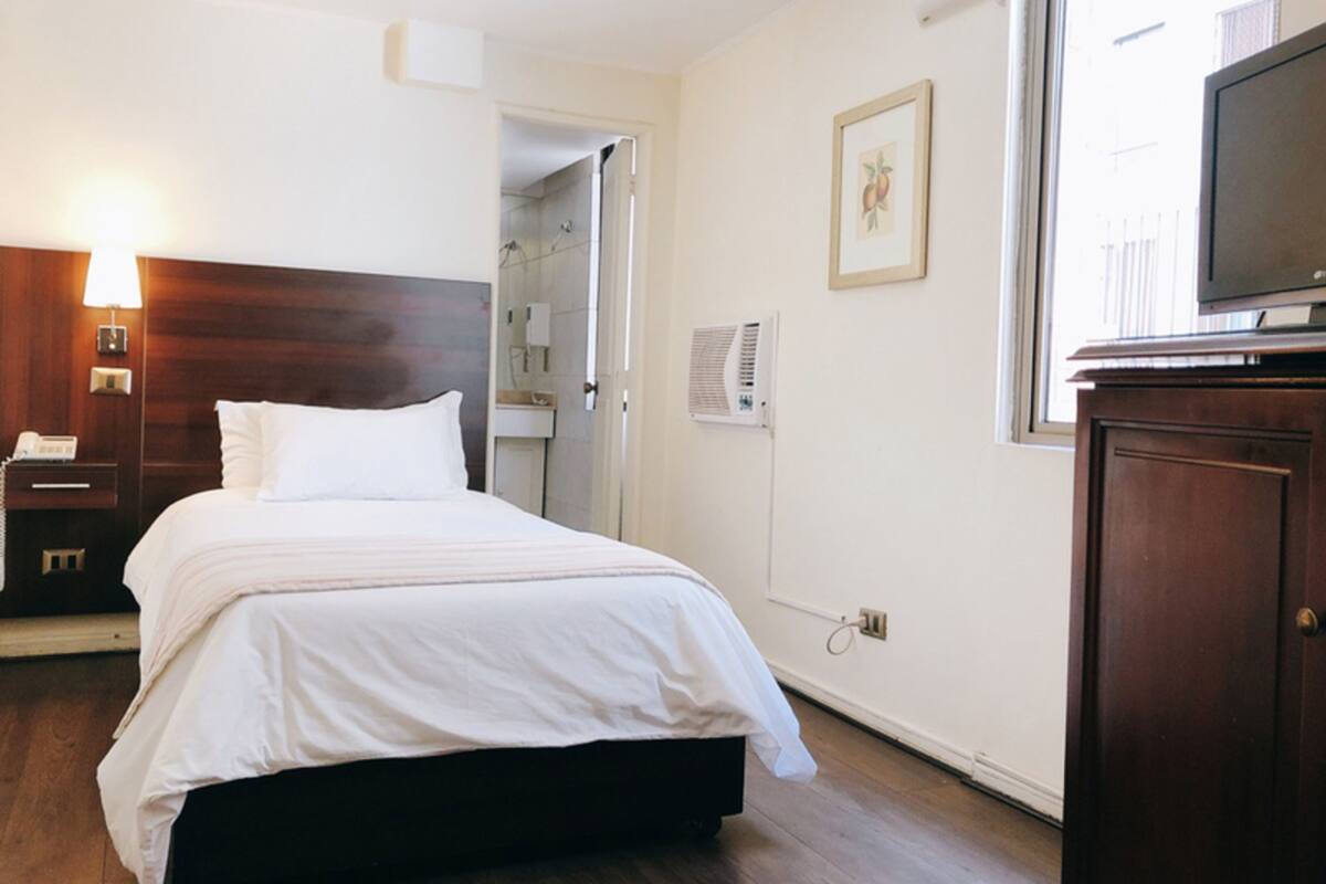 A hotel room with a bed, a bedside table with a lamp, a television on a cabinet, and a door leading to a bathroom.