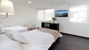 Habitación de hotel con dos camas, un escritorio, una lámpara, un cuadro en la pared y una ventana con persianas.