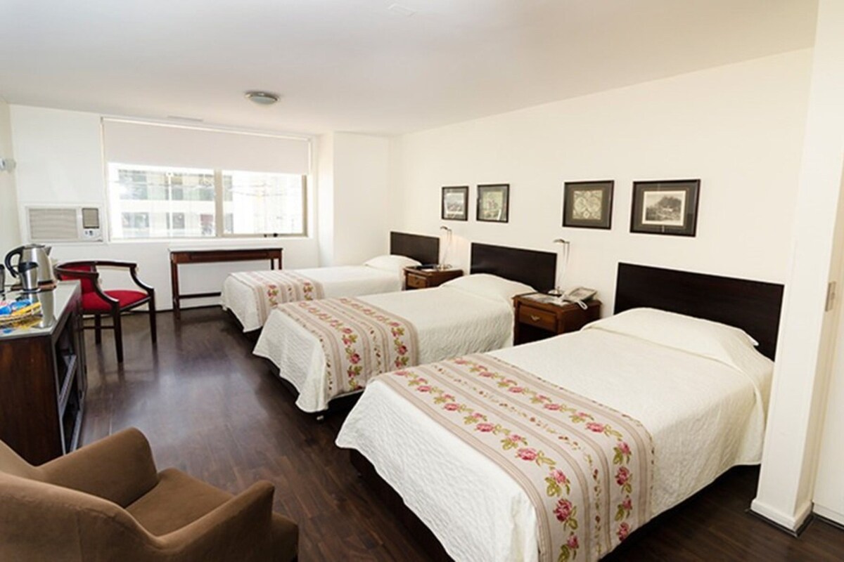 A hotel room with two beds, a desk, a chair, and a window.